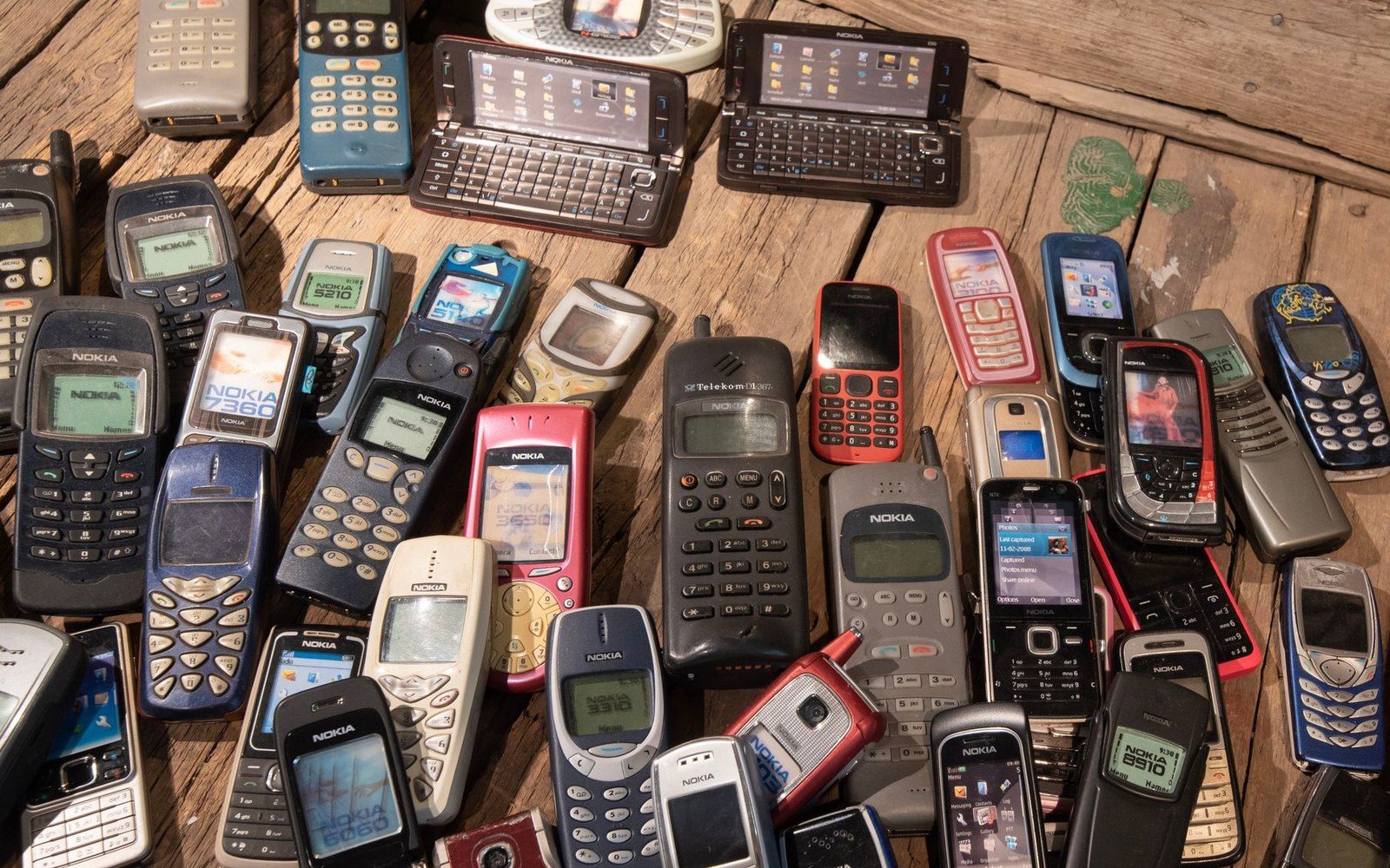 A row of early-2000s mobile phones — Nokia, Sony Ericsson, BlackBerry — arranged on a shelf