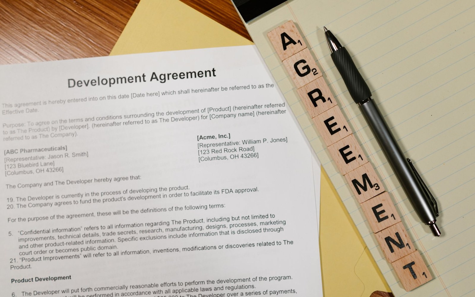 A printed development agreement document beside a pen and letter tiles spelling "agreement"