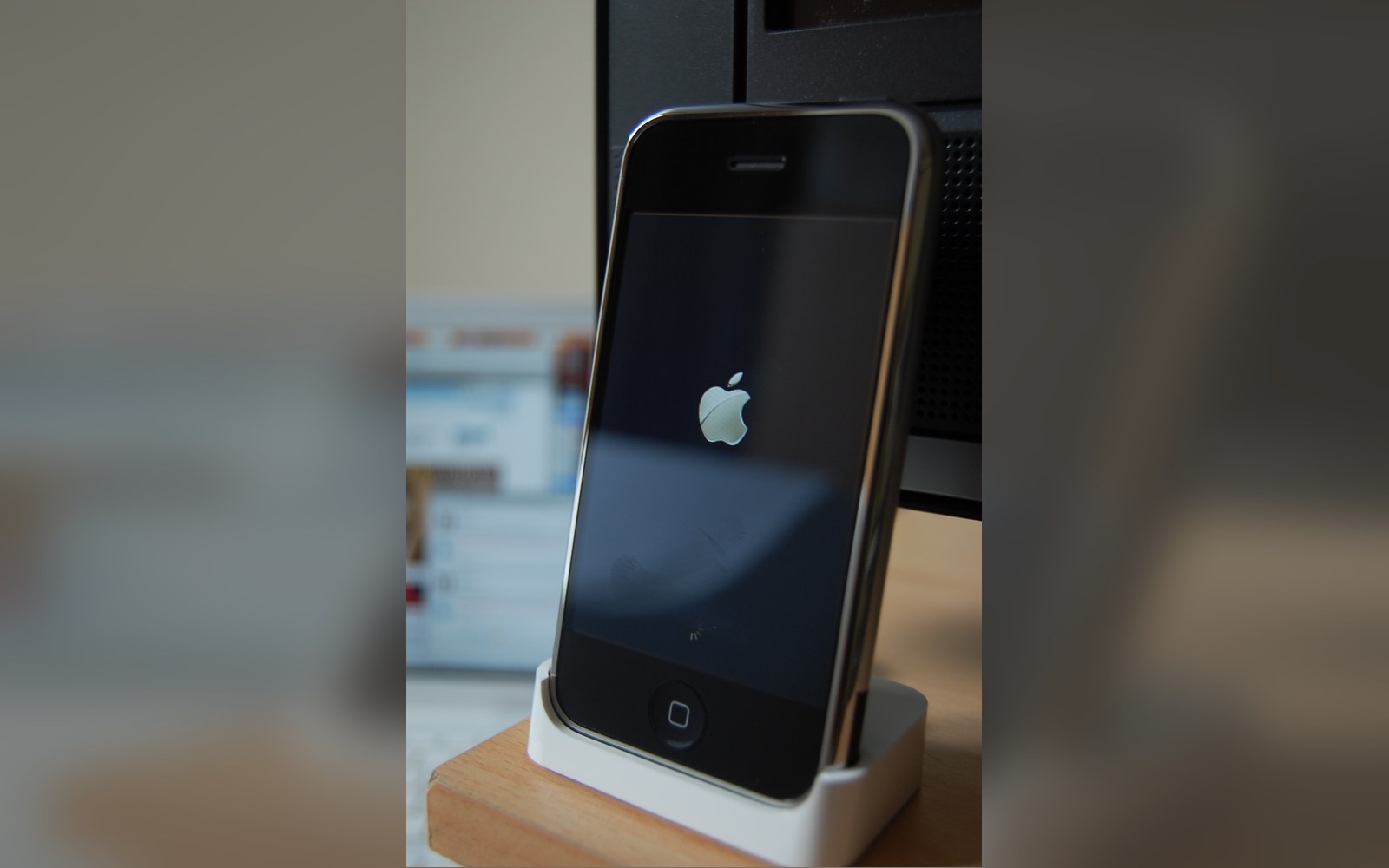 An original iPhone displaying the Apple logo while docked on a charging stand