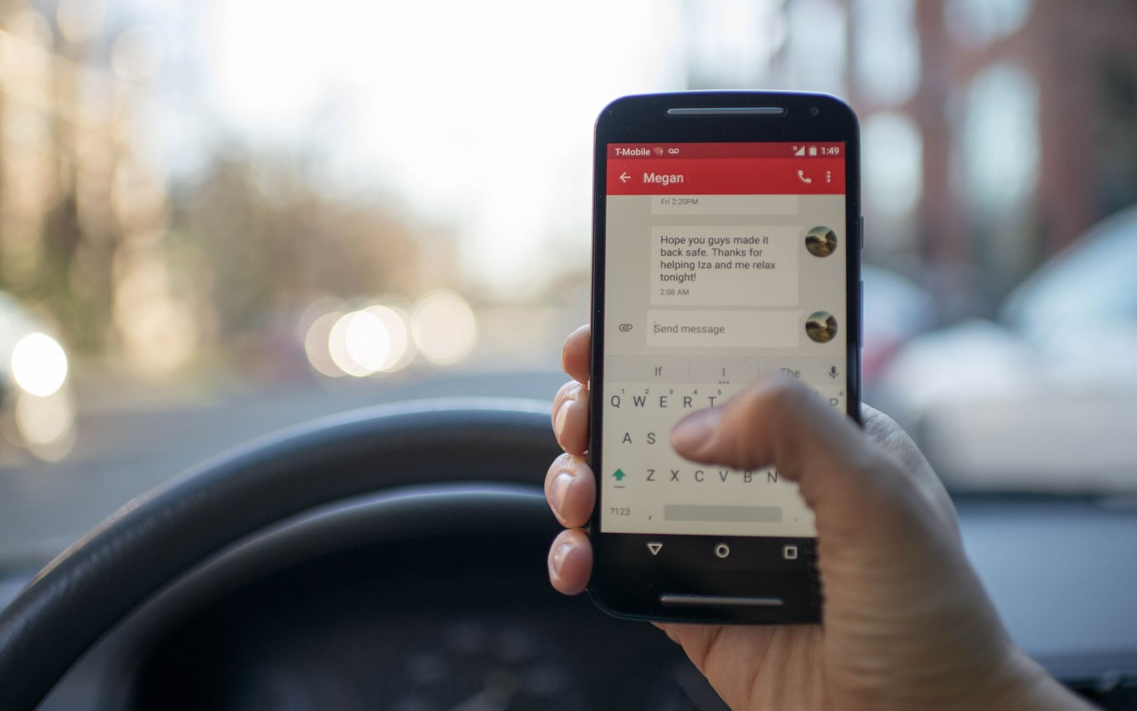 A driver holds a smartphone showing a text conversation while gripping the steering wheel