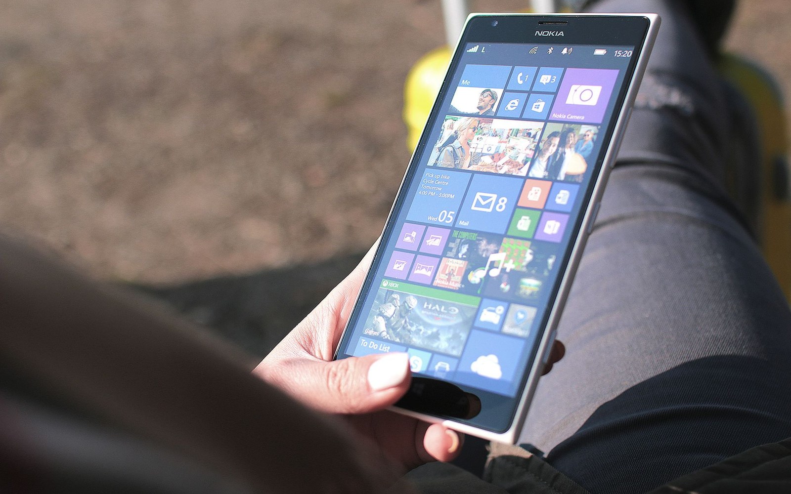 A hand holds a Nokia smartphone displaying its colorful Windows tile home screen