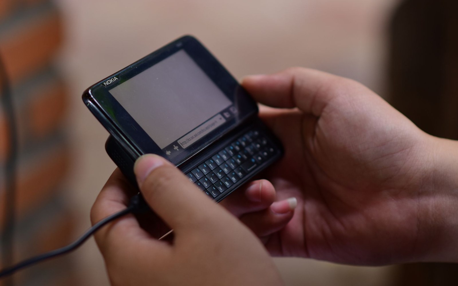 Hands holding an open Nokia slider phone with a slide-out qwerty keyboard