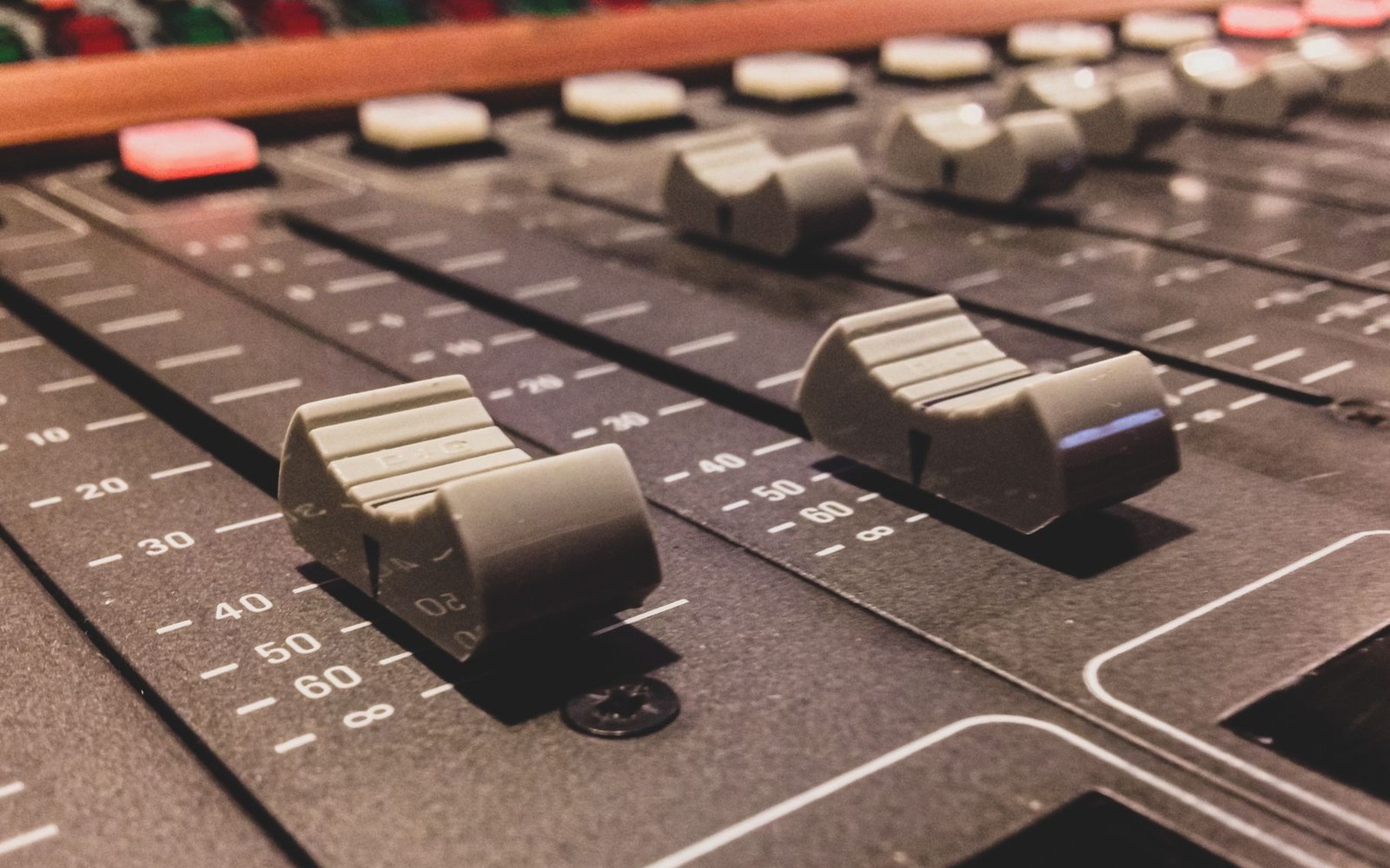 Close-up of sliding faders and marked gain scales on a mixing console