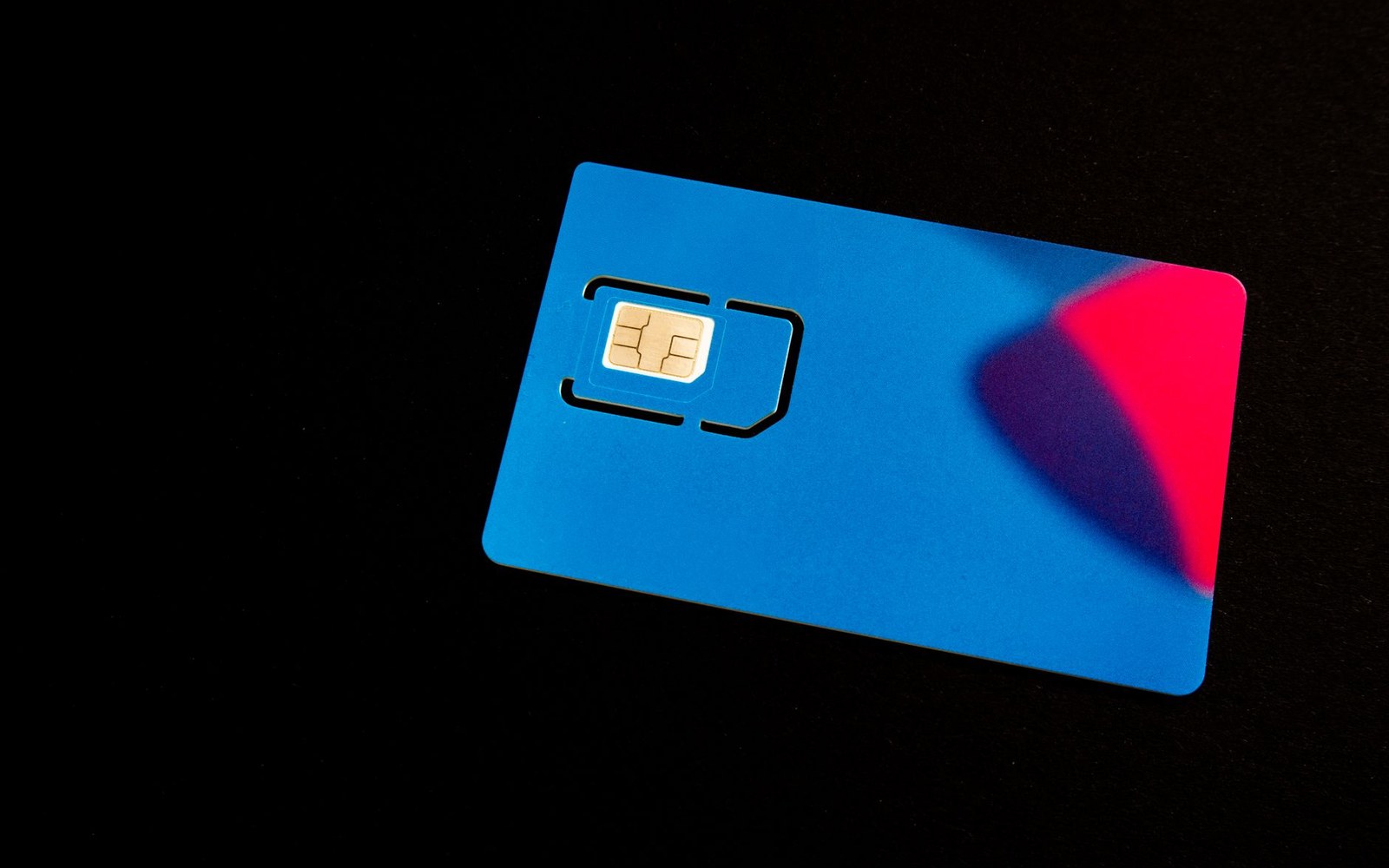 A blue SIM card with gold contacts lies on a black surface under red light