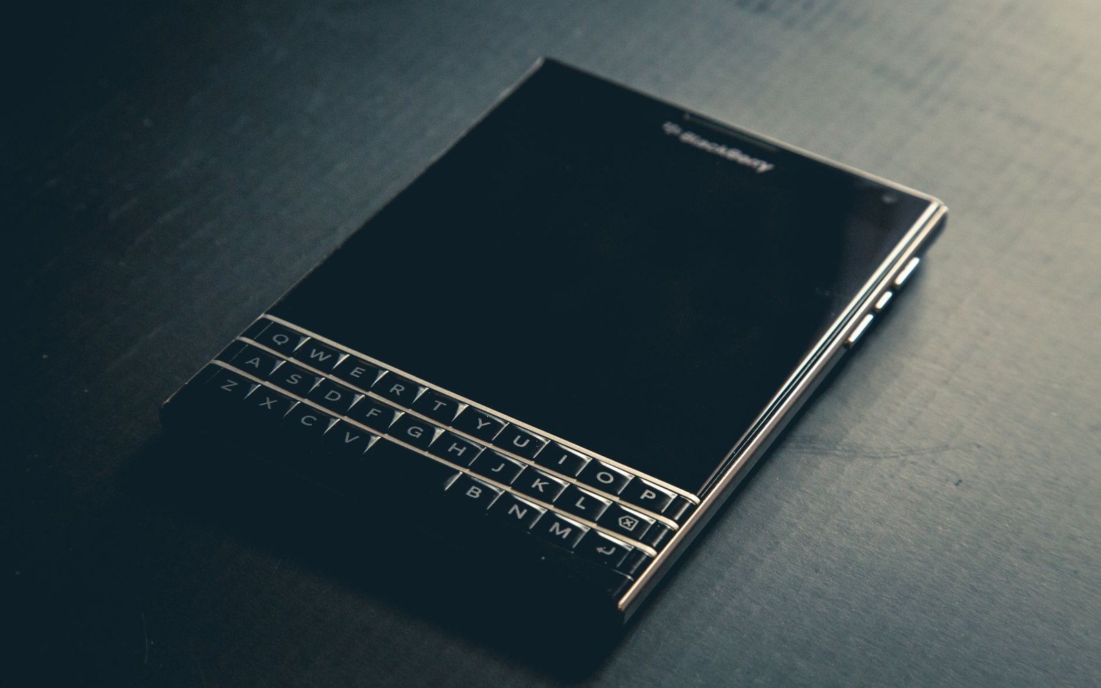 A blackberry passport smartphone with physical qwerty keyboard resting on a dark surface