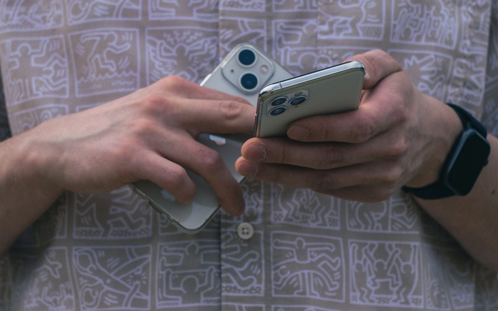 A person holds two smartphones stacked together while wearing a smartwatch