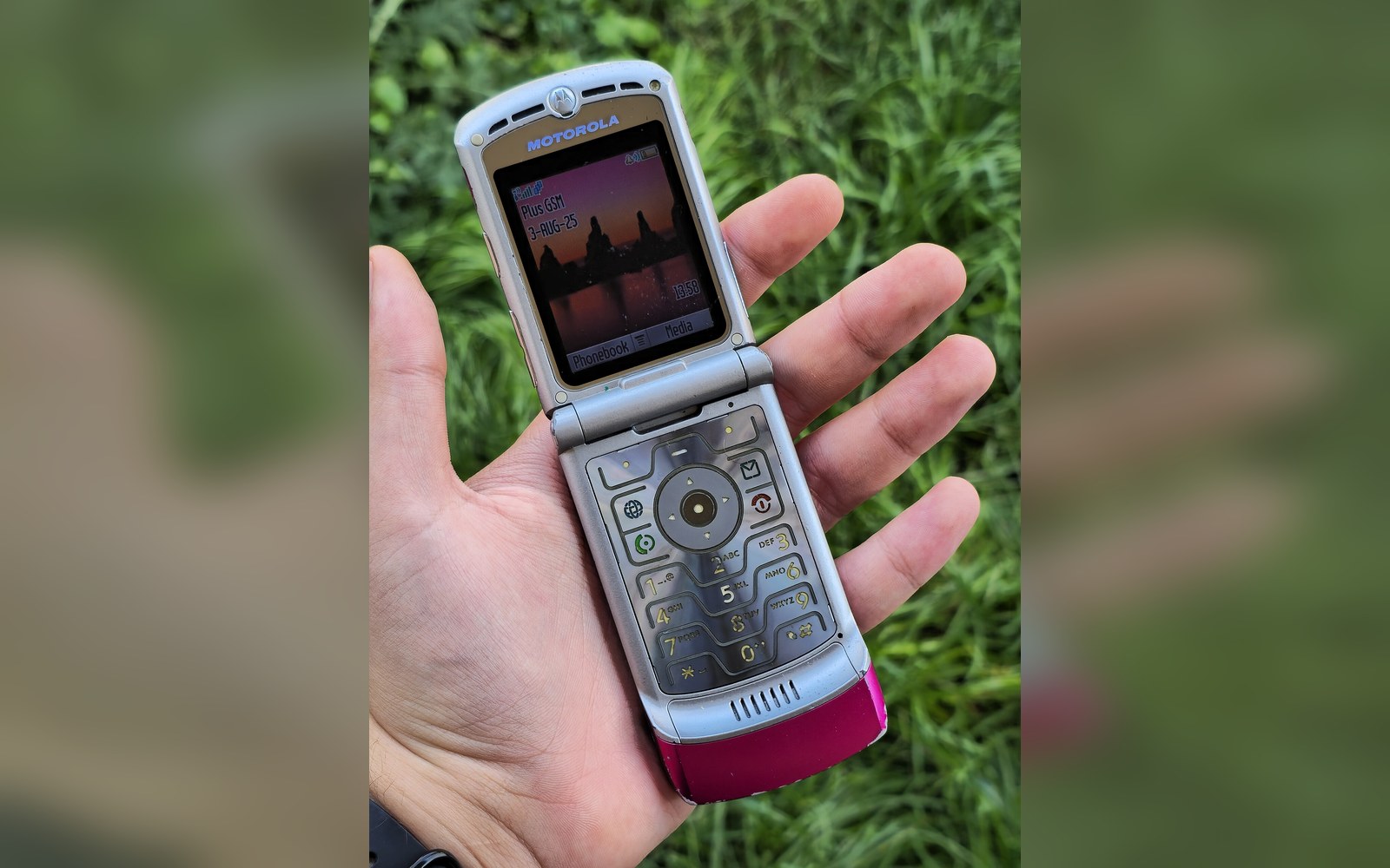 A Motorola Razr V3 half-open on a café table, an adult's hand reaching toward it